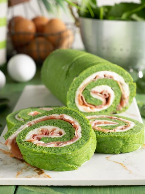 Rotolo di frittata agli spinaci affettato mostra la spirale di stracchino e speck