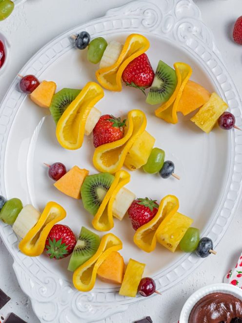 Spiedini di frutta con fragole, kiwi, uva, melone, ananas e peperone giallo su vassoio