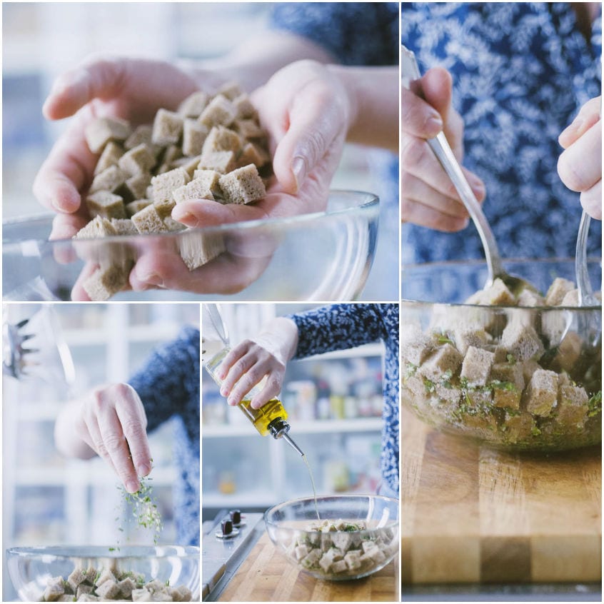 Cubetti di pane conditi con olio versato a filo, erbe tritate e sale in una ciotola