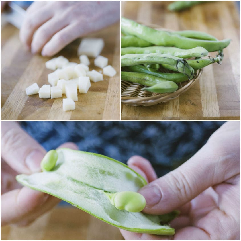 Mani che sgranano fave fresche dal baccello, accanto a cubetti di pecorino sul tagliere