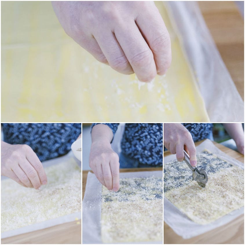 Mano che sparge Grana Padano grattugiato su sfoglia, poi sesamo e semi di papavero prima di tagliare i grissini