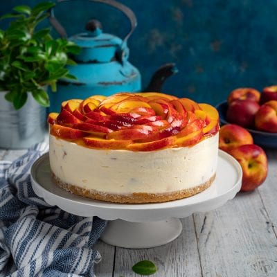 Cheesecake alle pesche con fette disposte a rosa sulla crema e base di biscotto