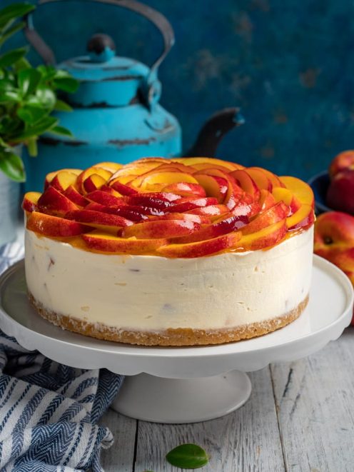 Cheesecake alle pesche con fette disposte a rosa sulla crema e base di biscotto