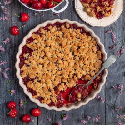 Crumble di ciliegie con briciole dorate e ripieno lucido di frutta, servito con un cucchiaio