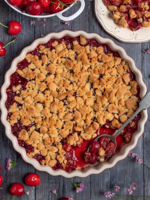 Crumble di ciliegie con briciole dorate e ripieno lucido di frutta, servito con un cucchiaio