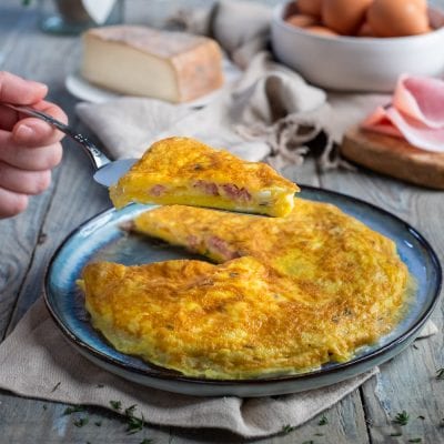 Frittata ripiena di cotto e taleggio con una fetta sollevata che mostra il ripieno filante