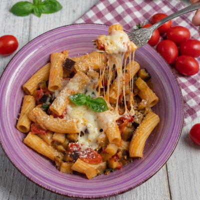 Pasta con le melanzane filante con mozzarella che si allunga sulla forchetta, pomodorini e basilico