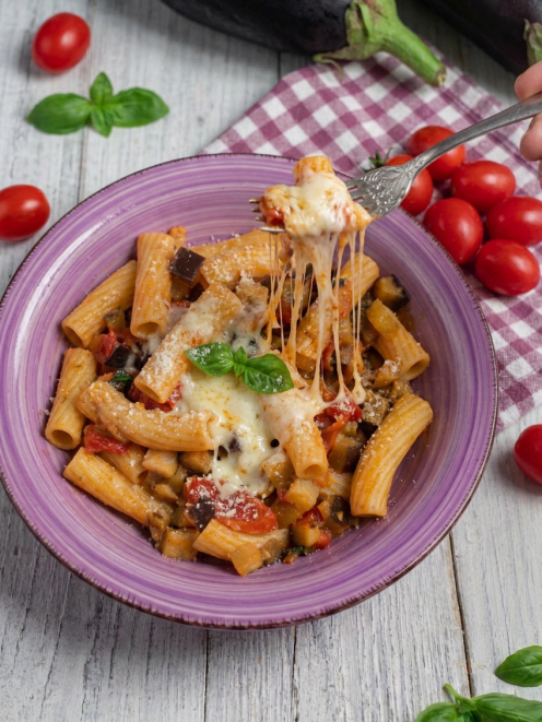 Pasta con le melanzane filante con mozzarella che si allunga sulla forchetta, pomodorini e basilico
