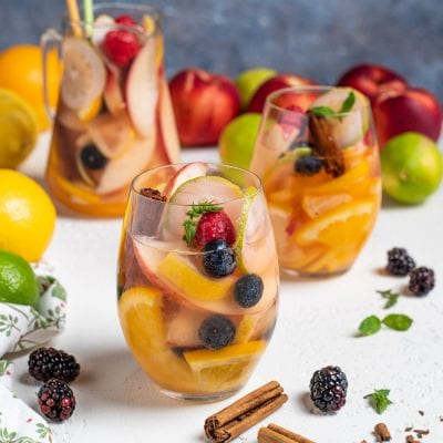 Sangria bianca con fette di arancia, mela, mirtilli e lamponi guarnita con cannella