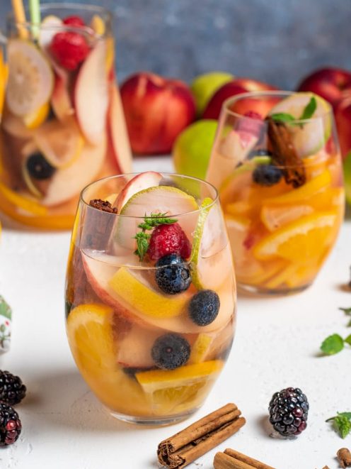Sangria bianca con fette di arancia, mela, mirtilli e lamponi guarnita con cannella