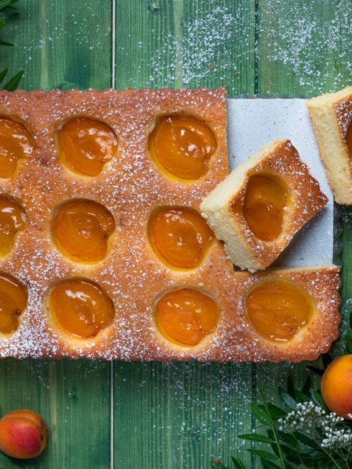 Torta di albicocche con mezze albicocche affondate nell'impasto e zucchero a velo, una fetta sollevata