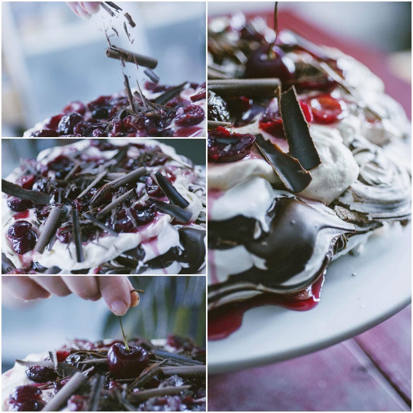 Mani che aggiungono scaglie di cioccolato e ciliegie sulla pavlova con panna e salsa ai frutti di bosco