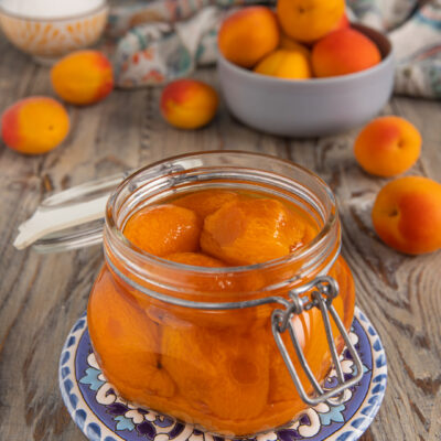 Albicocche sciroppate in barattolo di vetro aperto, con frutta fresca sullo sfondo