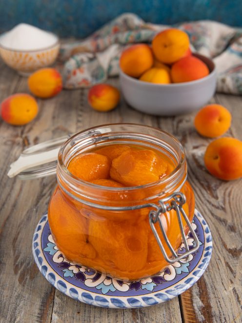 Albicocche sciroppate in barattolo di vetro aperto, con frutta fresca sullo sfondo