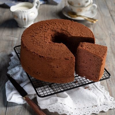 Chiffon cake al cacao spolverata di cacao amaro, con una fetta tagliata che mostra la mollica soffice