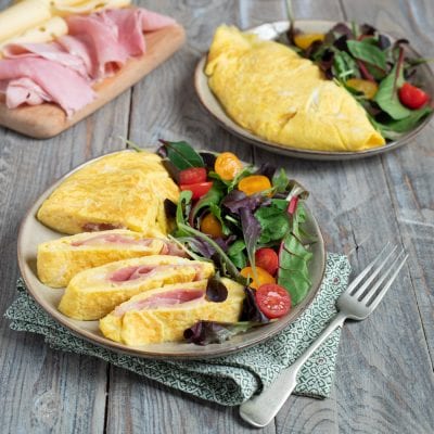 Omelette prosciutto e formaggio affettata, con il ripieno ben visibile, servita con insalata mista e pomodorini