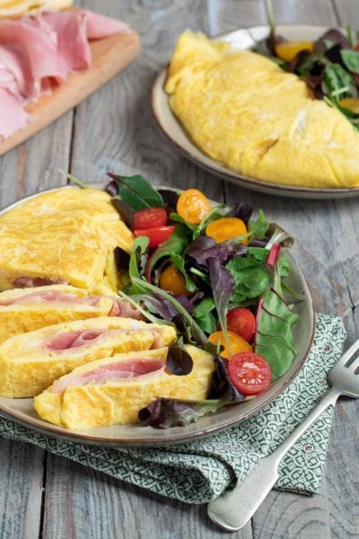 Omelette prosciutto e formaggio affettata, con il ripieno ben visibile, servita con insalata mista e pomodorini