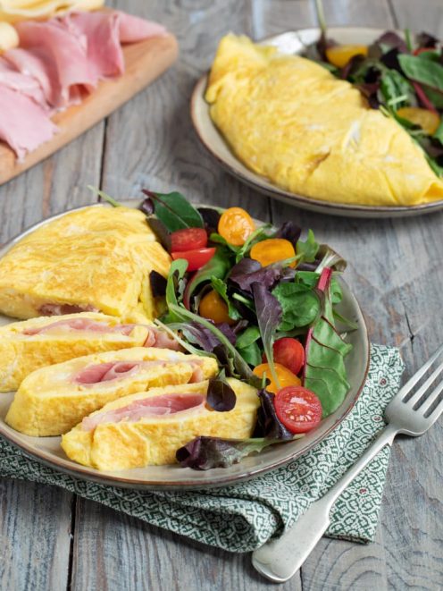 Omelette prosciutto e formaggio affettata, con il ripieno ben visibile, servita con insalata mista e pomodorini