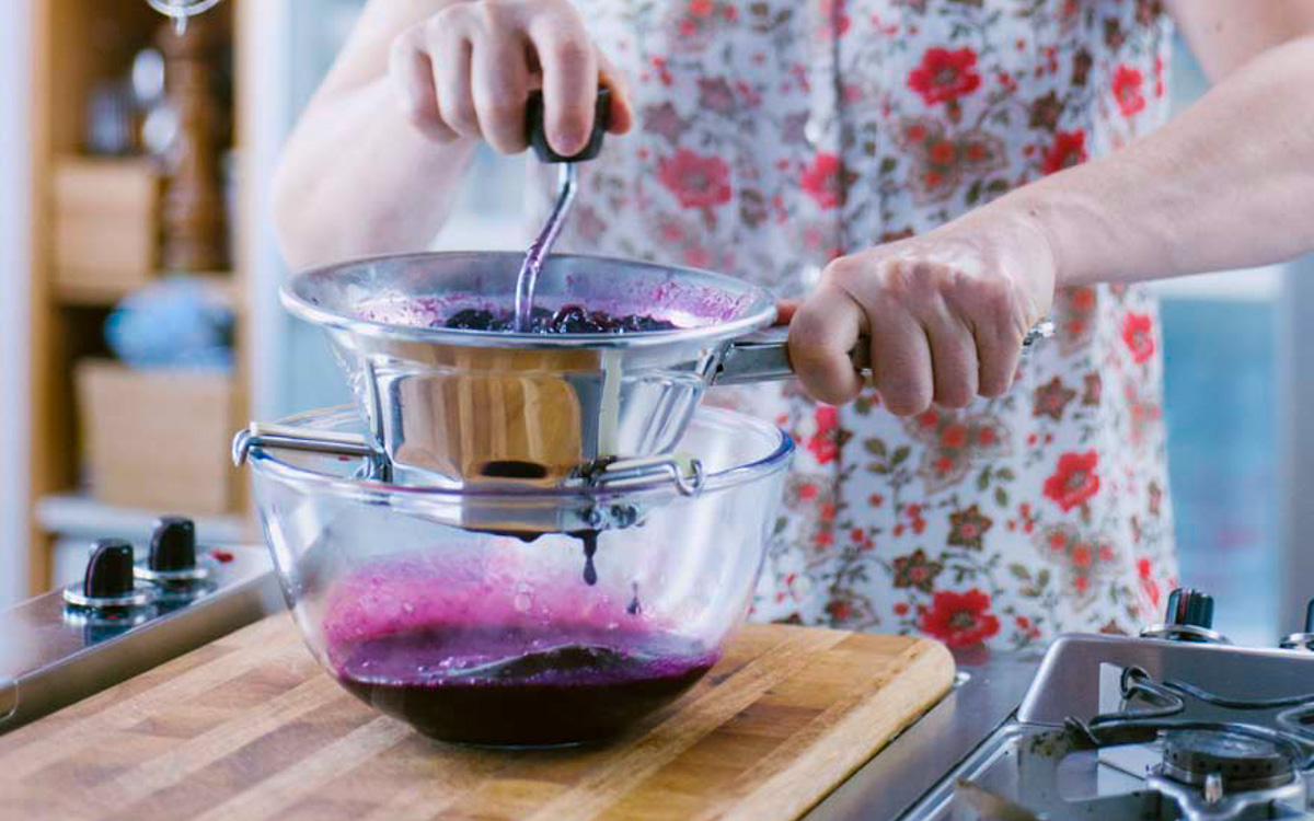 Passaggio dell'uva fragola cotta al passaverdure per ottenere una salsa viola liscia