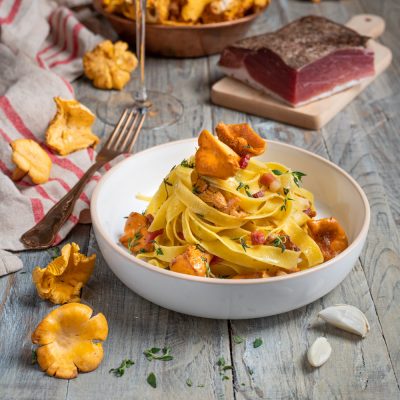 Tagliatelle con finferli e speck a cubetti, guarnite con timo fresco e un finferlo intero in cima