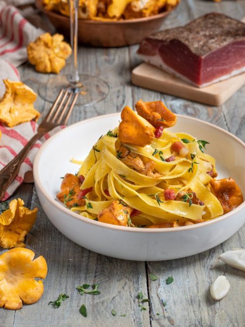 Tagliatelle con finferli e speck a cubetti, guarnite con timo fresco e un finferlo intero in cima