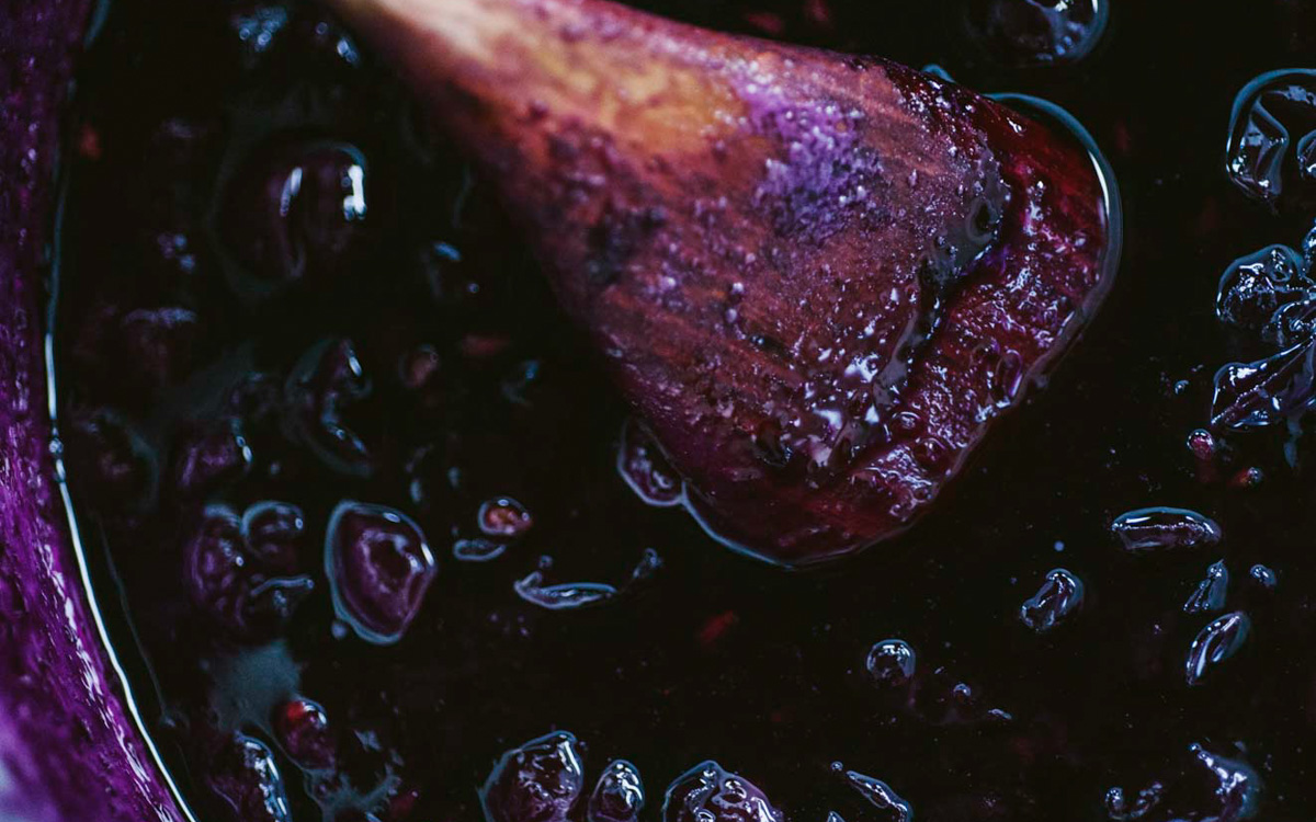 Composta di uva fragola che sobbolle nel tegame, mescolata con un cucchiaio di legno