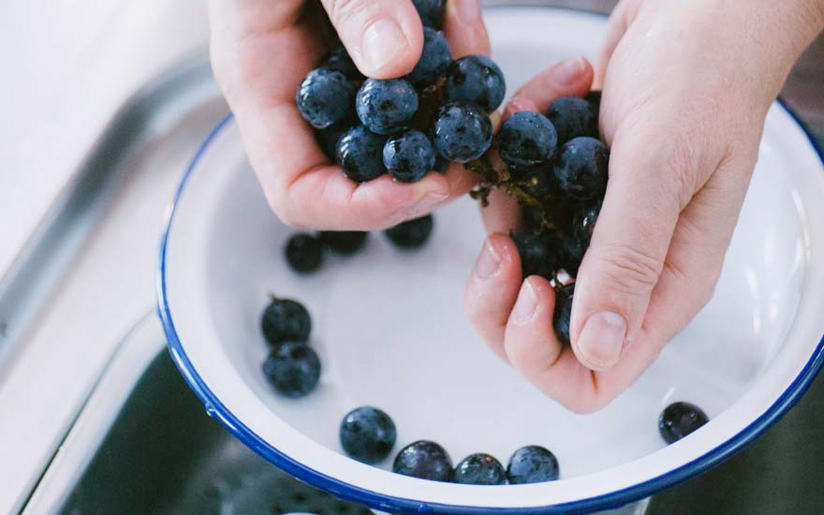 Mani che sgranano acini di uva fragola bagnata sopra una ciotola