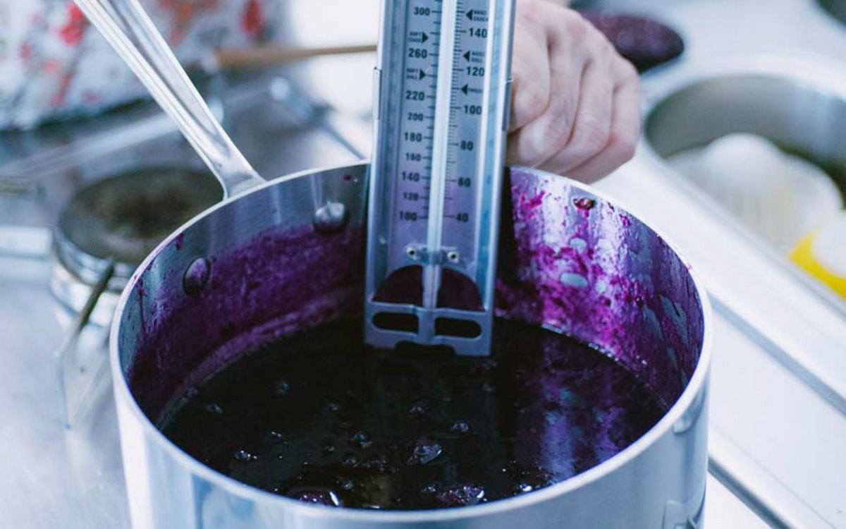 Termometro da cucina immerso nella confettura di uva fragola in cottura