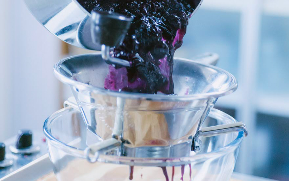 Composto di uva fragola cotto versato nel passaverdure per separare polpa da bucce e semi