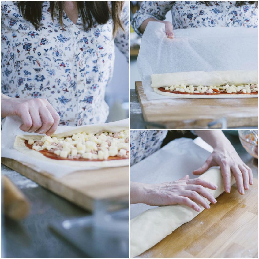 Mani che arrotolano l'impasto farcito con salsa, formaggio e salsiccia per formare il rotolo di pizza