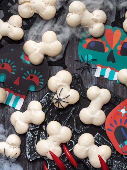 Ossa di Halloween a forma di osso disposte su un piano scuro con decorazioni teschio colorate