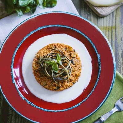 Couscous alla Norma con fonduta di caciocavallo, guarnito con julienne di zucchine e foglie di basilico