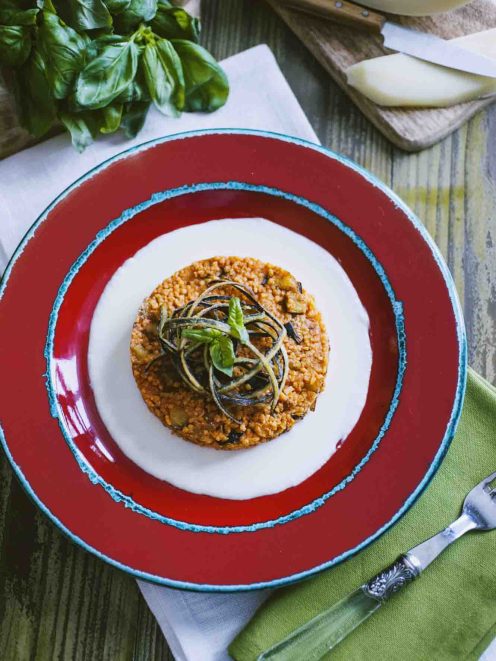 Couscous alla Norma con fonduta di caciocavallo, guarnito con julienne di zucchine e foglie di basilico