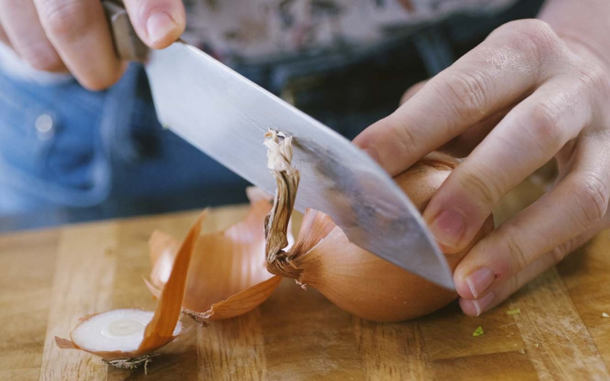 Mani che tagliano a metà una cipolla dorata con un coltello da chef