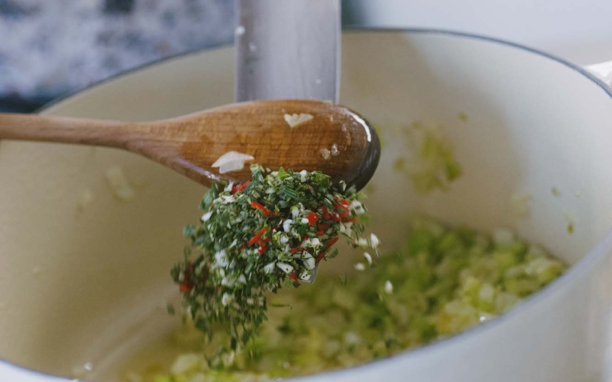 Trito di erbe aromatiche, aglio e peperoncino versato con un cucchiaio di legno nel soffritto