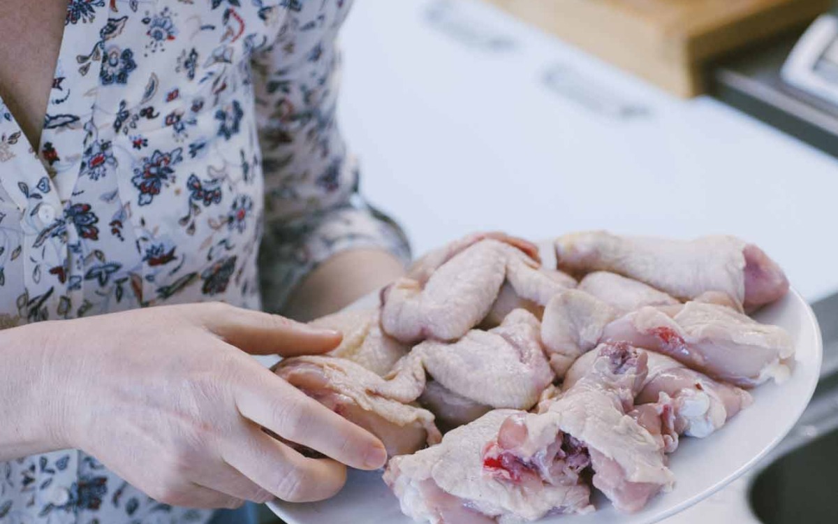 Mani che reggono un vassoio con pezzi di pollo crudo pronti per la preparazione