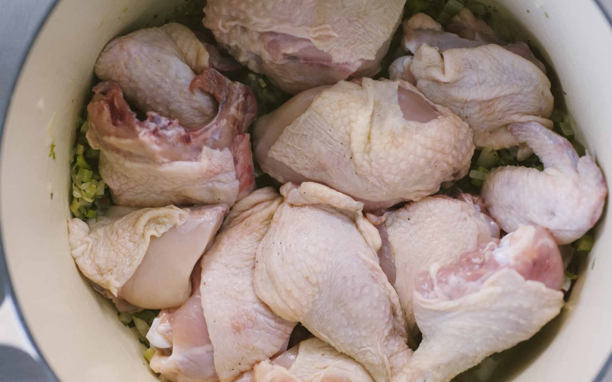 Pezzi di pollo crudo adagiati su un soffritto di verdure prima della rosolatura