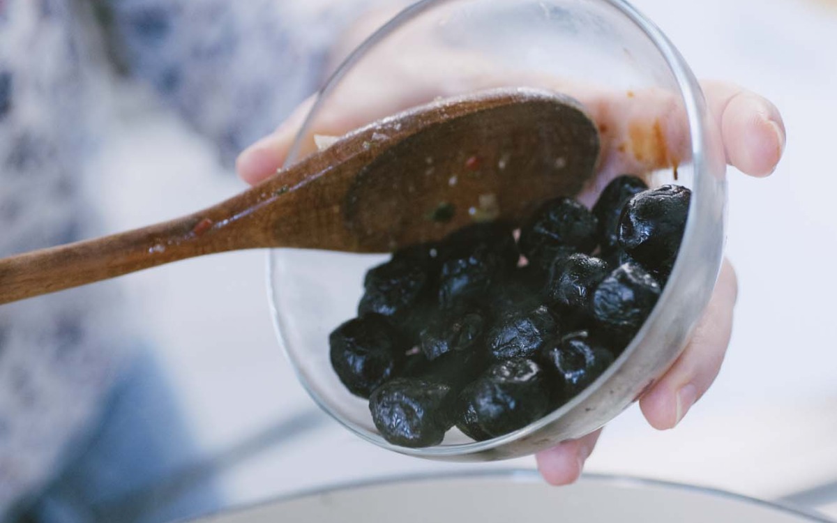 Olive nere schiacciate versate con un cucchiaio di legno nel tegame per il pollo alla cacciatora