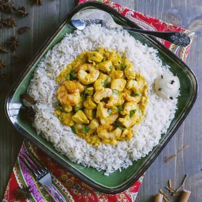 Pollo e gamberi al curry adagiati su un letto di riso pilaf con foglie di coriandolo