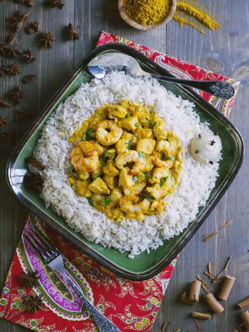 Pollo e gamberi al curry adagiati su un letto di riso pilaf con foglie di coriandolo