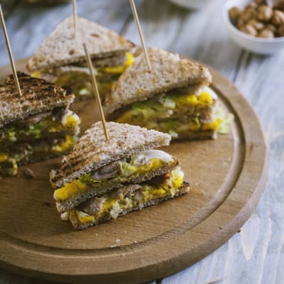 Tramezzino con sgombro e uova tagliato a metà, con ripieno giallo e verdure, fissato con stecchini