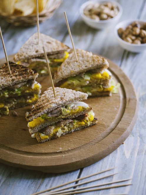 Tramezzino con sgombro e uova tagliato a metà, con ripieno giallo e verdure, fissato con stecchini