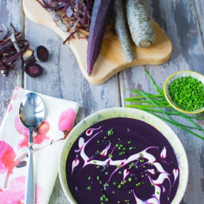 Vellutata di carote viola con swirl di panna e erba cipollina tritata, servita con carote crude sul tagliere