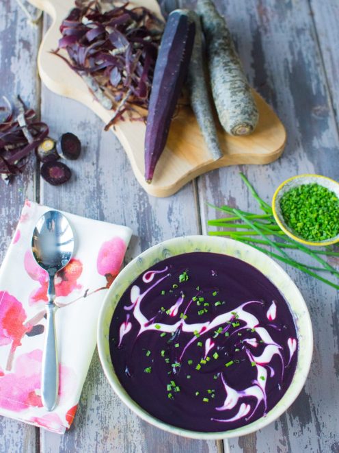 Vellutata di carote viola con swirl di panna e erba cipollina tritata, servita con carote crude sul tagliere