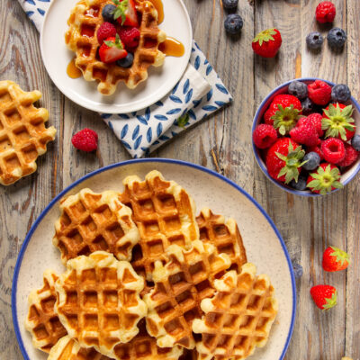 Waffle belgi dorati impilati, uno guarnito con fragole, lamponi, mirtilli e sciroppo d'acero