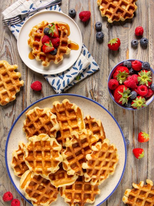 Waffle belgi dorati impilati, uno guarnito con fragole, lamponi, mirtilli e sciroppo d'acero