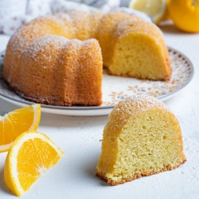 Dolce presto fatto a ciambella con zucchero a velo, una fetta in primo piano e spicchi d'arancia