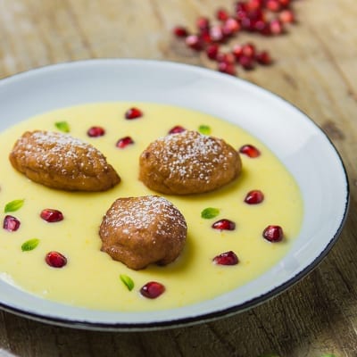 Frittelline di couscous adagiate su crema pasticcera, guarnite con chicchi di melograno e foglioline di menta