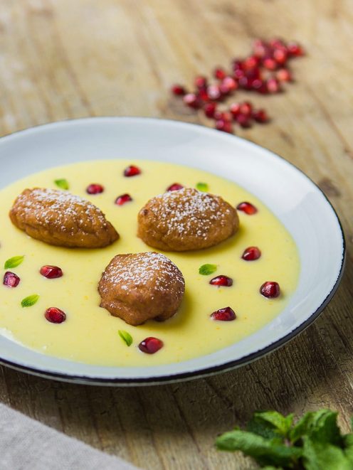 Frittelline di couscous adagiate su crema pasticcera, guarnite con chicchi di melograno e foglioline di menta