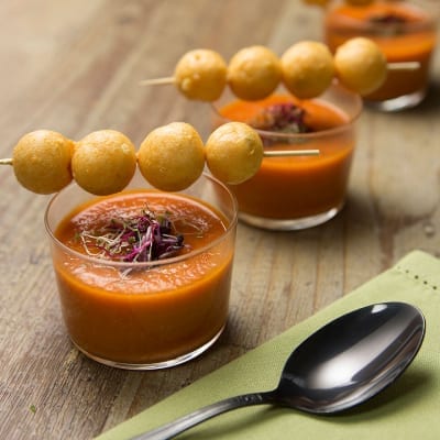 Meringhe salate con gazpacho servito in bicchiere, guarnito con microgreens e spiedino di palline dorate